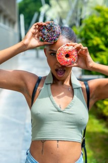 Young woman playfully covering her eyes with two colorful donuts, posing with an open mouth and
