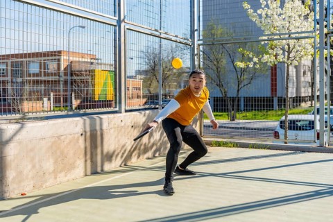 Young athletic man lunging with a paddle to strike a yellow ball on an outdoor pickleball court,