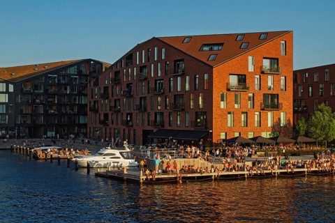 Backsteingebäude bei Sonnenuntergang umgeben von Wasser und Menschen an einem Hafen, Kopenhagen