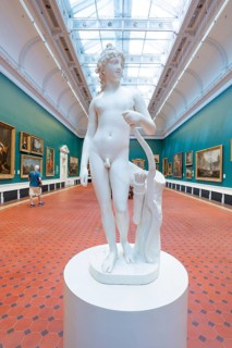 Marble sculpture of a naked man in an art gallery with blue walls and paintings, National Gallery
