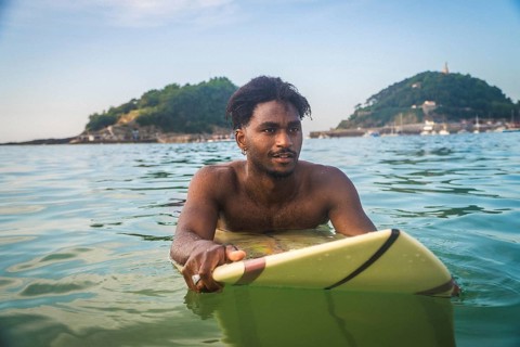 Man paddling on a surfboard in san sebastian, enjoying a summer day at the beach with mountains and