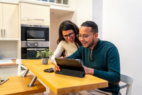 Happy couple smiling and watching content on a digital tablet in their modern home kitchen, sharing