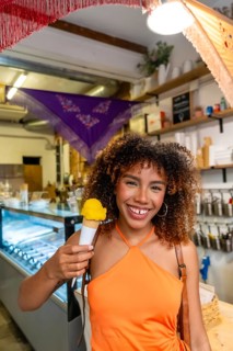 Young afro brazilian woman with curly hair smiling and holding a refreshing yellow ice cream cone,