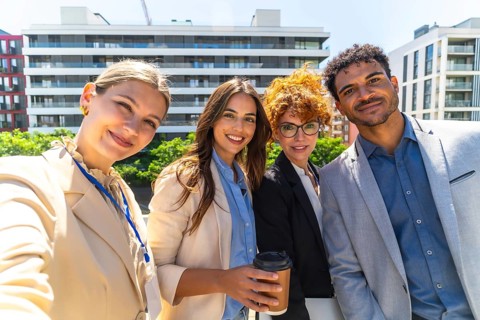 Happy diverse business team smiling and taking a rooftop selfie during a coffee break, celebrating