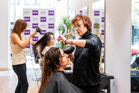Professional hairstylists providing hair care services to female customers, using hairdryers to dry