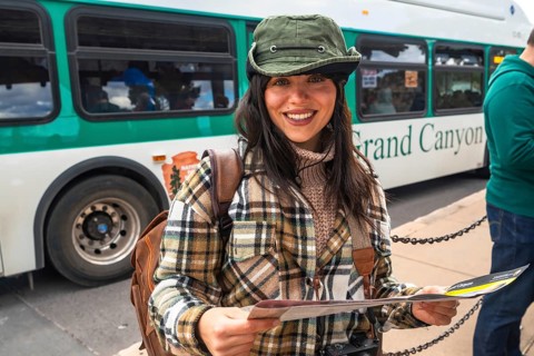 Young woman tourist smiling and holding a park map while waiting at a grand canyon national park
