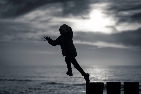 Silhouette of boy jumping from breakwater stilt during sunset