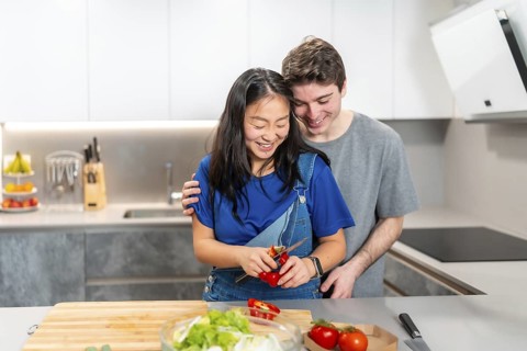 Multiethnic couple enjoying a cooking session at home. Smiling while preparing fresh vegetables on