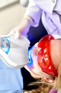 A dental clinic professional performs a teeth whitening procedure using advanced equipment. The