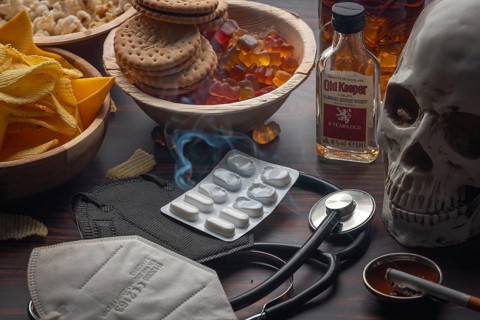 Tablets and stethoscope with skull and crossbones next to unhealthy food and cigarette