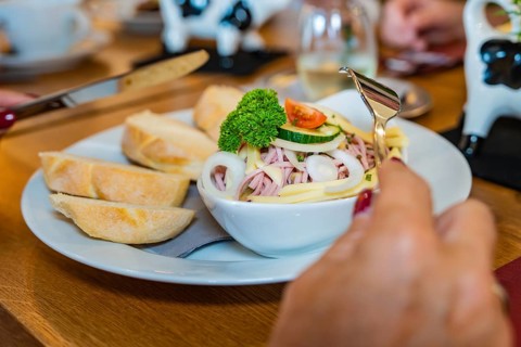 Sausage salad with onions, gherkins and tomatoes, served with bread. One hand holds a fork, autumn
