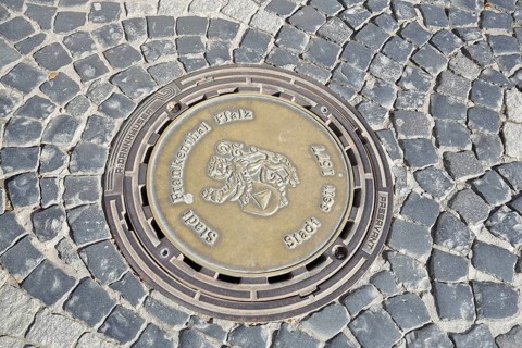 Round manhole cover with city coat of arms and date 1577 for granting city rights, inscription,