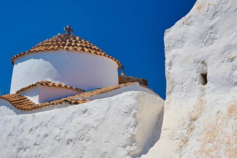 White church with red tiled roof and cross on top, in front of a clear blue sky, Chora, Old Town,
