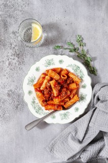 Rigatoni pasta with meat sauce and parmesan cheese on a light table, top view, homemade, no people