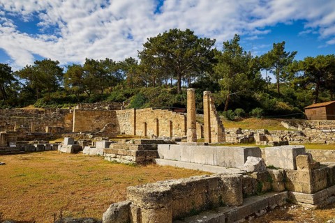 Ancient ruins with columns and stone walls in sunny weather with trees in the background, Kamiros,