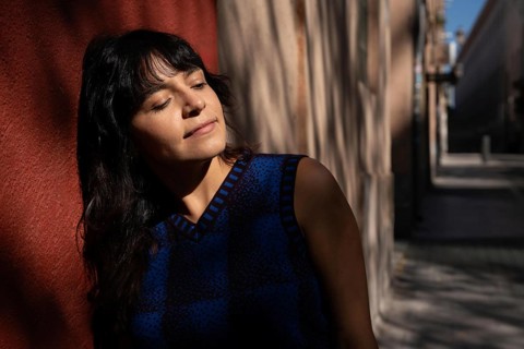 A Latin woman tilts her face towards the sun with her eyes closed, embracing a peaceful moment