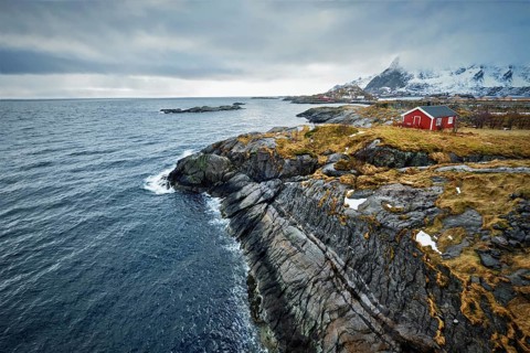 Clif with traditional red rorbu house on Litl-Toppoya islet on Lofoten Islands, Norway in winter