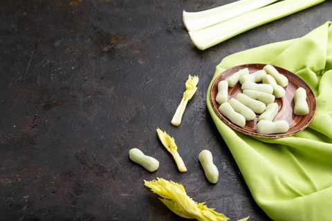 Jelly celery candies on black concrete background and green linen textile. copy space, side view