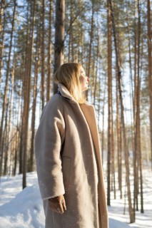 A woman experiences a serene moment in a sunny winter forest, feeling the warmth of sunlight on her