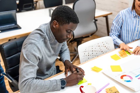 African man writing ideas in a note during brainstorming meeting in a modern coworking