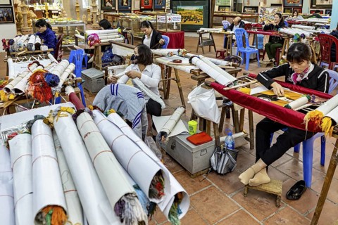 Women work in a room on traditional embroidery with colourful yarns and fabric rolls, painters and