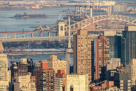 Aerial view of New York City's bustling landscape with the prominent Hell Gate Bridge and RFK