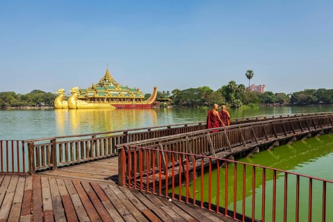 YANGON, MYANMAR, JANUARY 3, 2014: Two Buddhist monks walking on wooden bridge at at Kandawgyi Lake