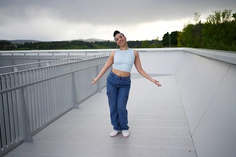 A woman in blue jeans and a blue top is standing on a white surface. She is smiling and she is