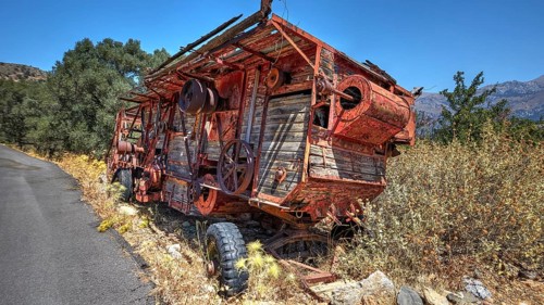 Abandoned, rusty machine next to a road with lush vegetation and mountain views in the background,