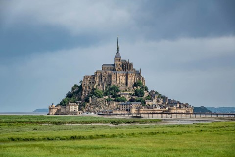 View over lush green salt marshes to the rocky island, Le Mont Saint Michel monastery island with