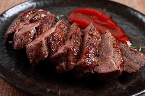 Roast duck breast, sliced on a plate, with red sauce, homemade, no people