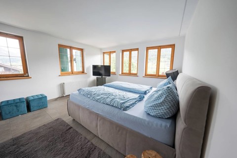 Modern bedroom with large double bed and blue bed linen, windows flood the room with light, holiday
