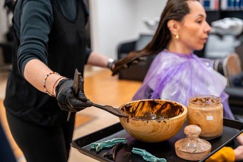 Hairdresser applying natural brown henna dye mixture onto a woman's hair in a salon, preparing for
