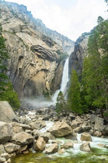Powerful lower yosemite fall plunges from a granite cliff, sending mist over boulders and flowing
