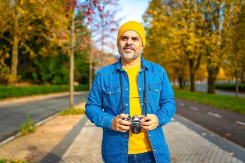 Male mature modern tourist walking along a city carrying digital camera in autumn