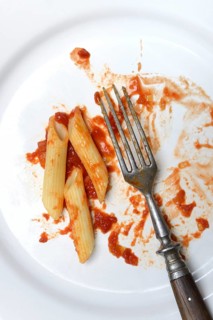 Plate with fork and leftover pasta, penne and tomato sauce, food waste