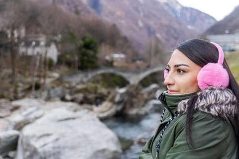 A woman with pink earmuffs gazes at the picturesque Ponte Dei Salti bridge in Lavertezzo, Ticino,