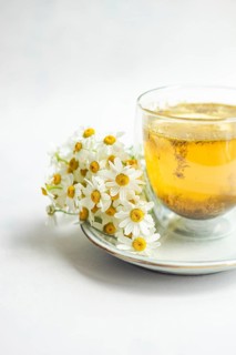 A delicate cluster of white daisies rests beside a steaming cup of chamomile tea on a pristine