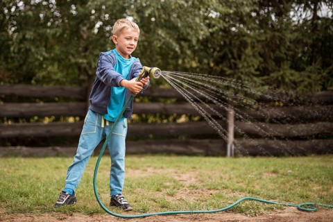Young boy watering grass in the garden