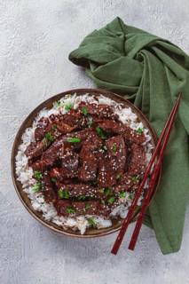Crispy beef, with green onions and sesame seeds, on a rice pad, in a bowl with chopsticks, on a