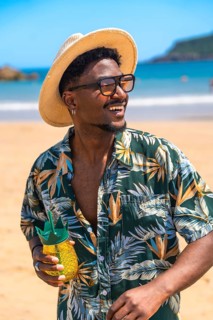Young man wearing stylish sunglasses and a trendy hat, savoring a refreshing cocktail while