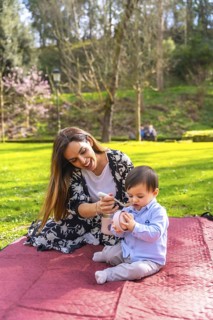 Happy mother feeding her baby boy solid food from a thermos while having a picnic in a park