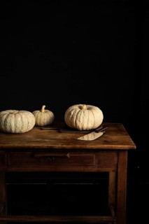 Three pumpkins rest on a rustic wooden table beside a knife, set against a dark background. The