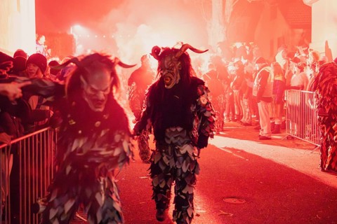 People in frightening costumes take part in a night-time festival under red light, carnival,