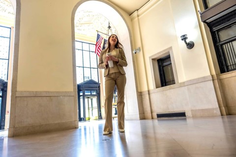 Young professional woman entering an arched hallway, holding a take out coffee cup, smiling and