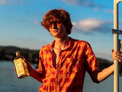 Young man standing by the lake, holding a bottle of alcohol in his hands, Jägermeister herbal
