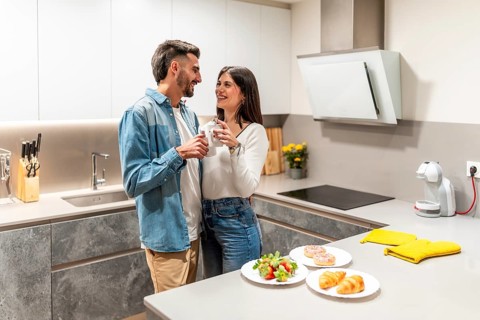 Young couple embracing and drinking coffee in their modern kitchen, with breakfast pastries and