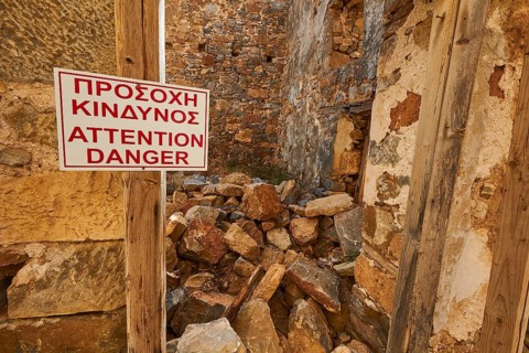 Sign warning of danger amidst ruins with scattered stones and wooden frames, Venetian sea fortress,