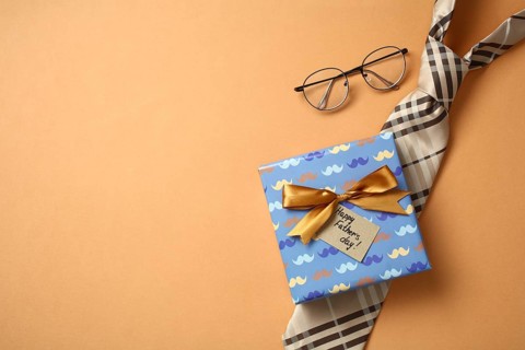 From above, a well wrapped Father's Day gift with a tie and glasses craftily arranged on a orange