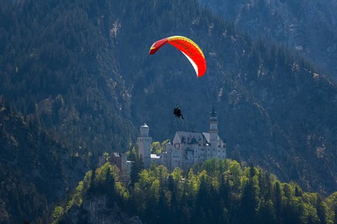 A paraglider glides over Neuschwanstein Castle against a mountainous backdrop, tandem, Schwangau